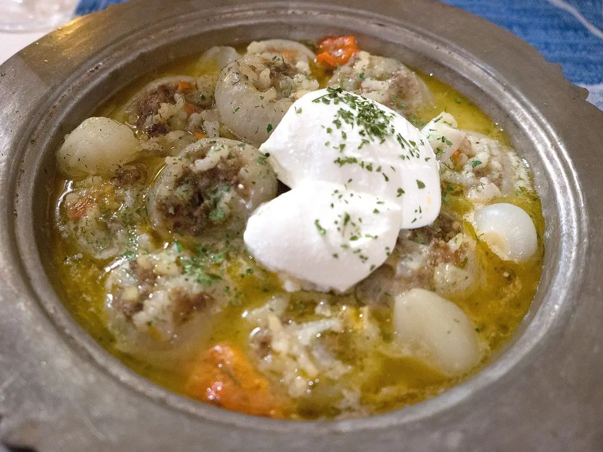 Cebollas rellenas de carne en una cazuela metálica con yogur y hierbas por encima