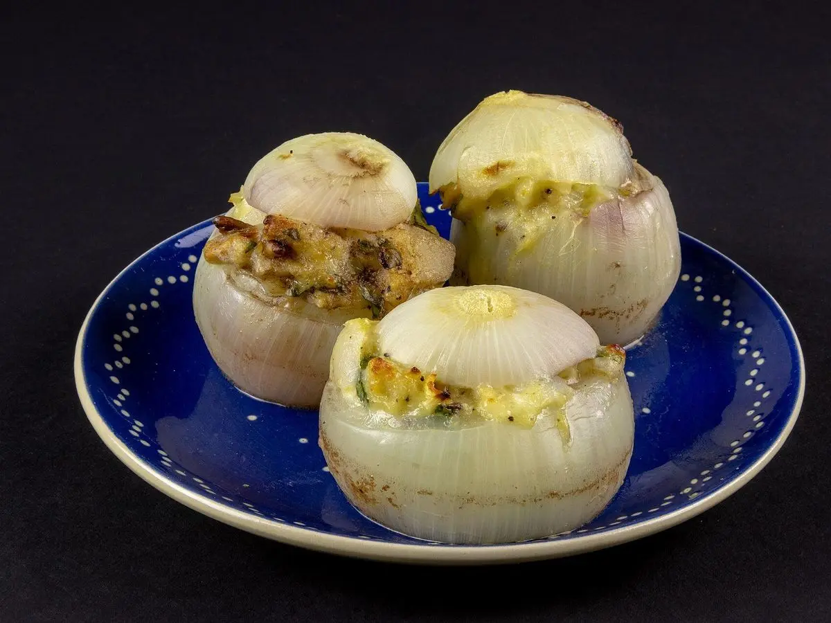 Tres cebollas enteras vaciadas y rellenas, gratinadas al horno, en un plato azul sobre fondo oscuro