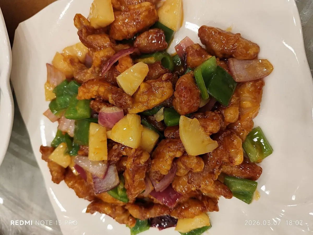 Cerdo rebozado en salsa agridulce con trozos de piña y pimiento verde en un plato blanco