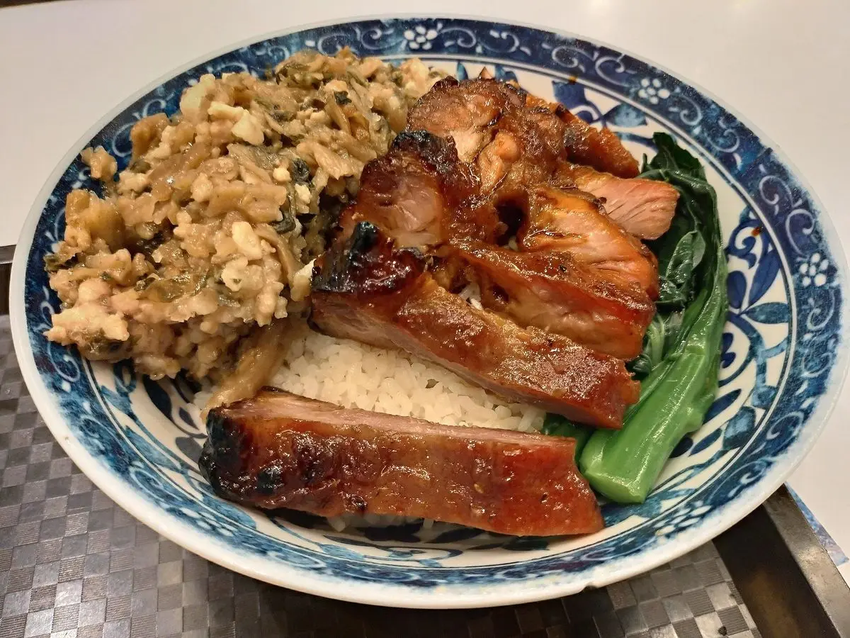 Lonchas de cerdo char siu glaseado con arroz y verdura verde en un plato de porcelana azul
