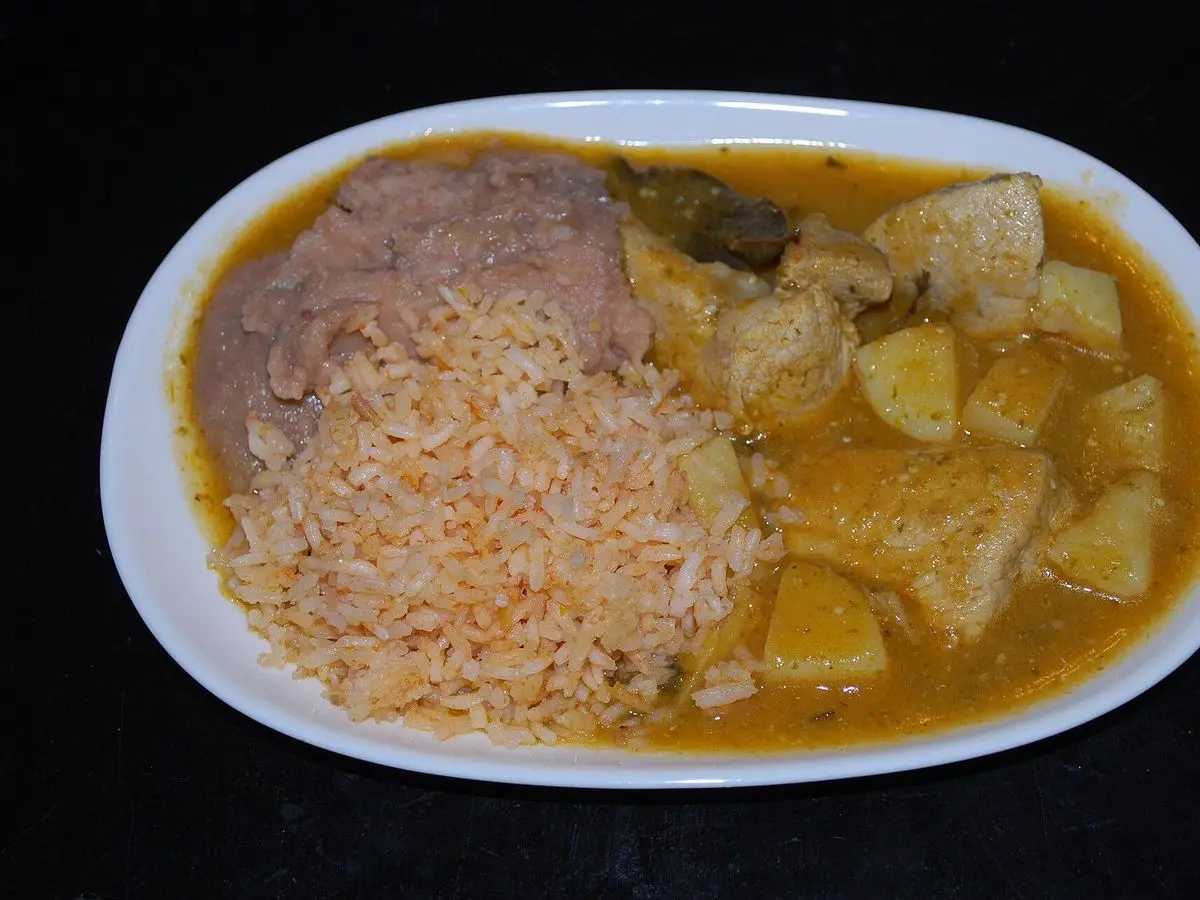 Plato ovalado con cerdo en salsa verde con verduras, arroz rojo y frijoles refritos