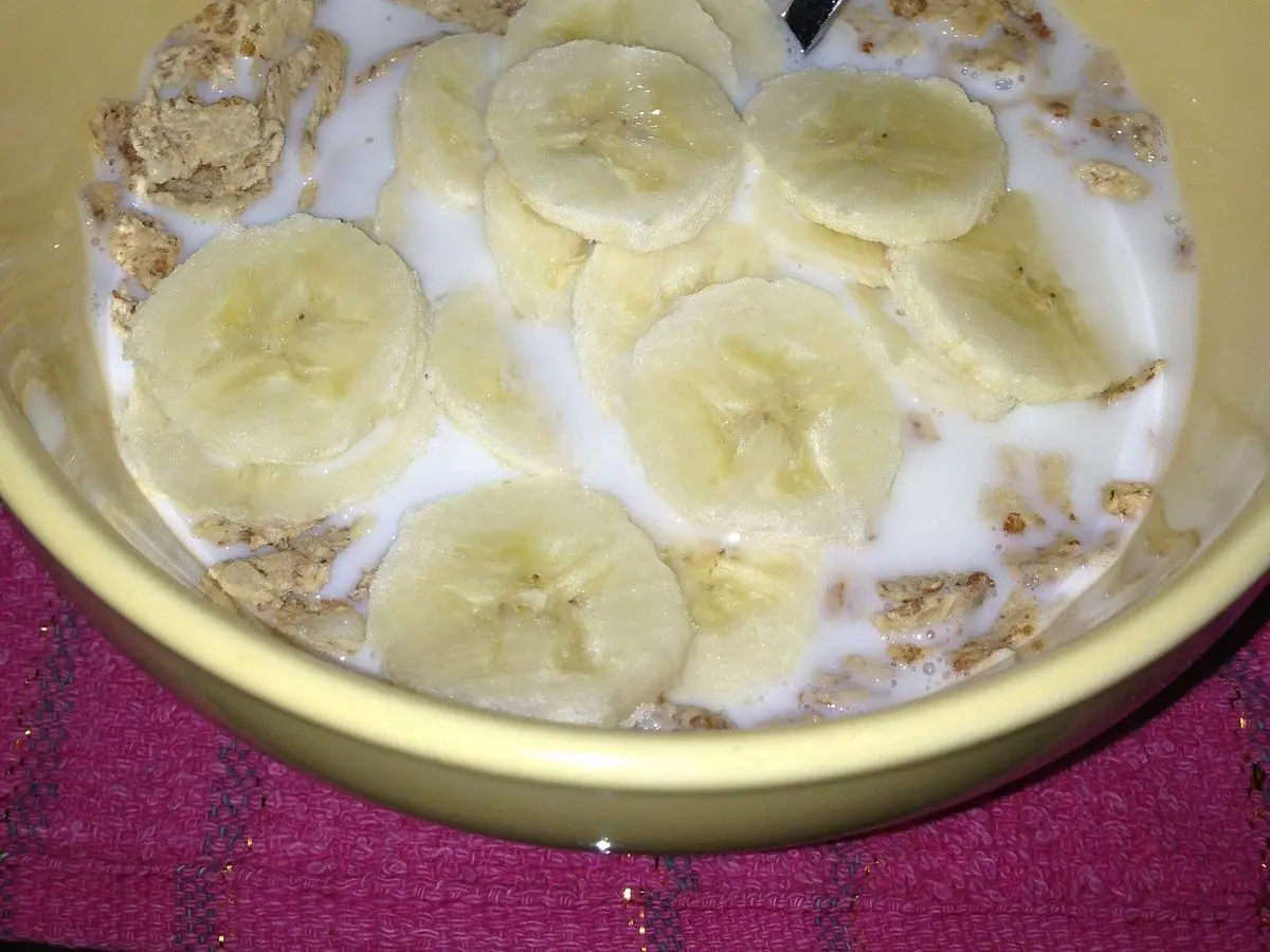 Cuenco amarillo de cereales con leche y rodajas de plátano con una cuchara