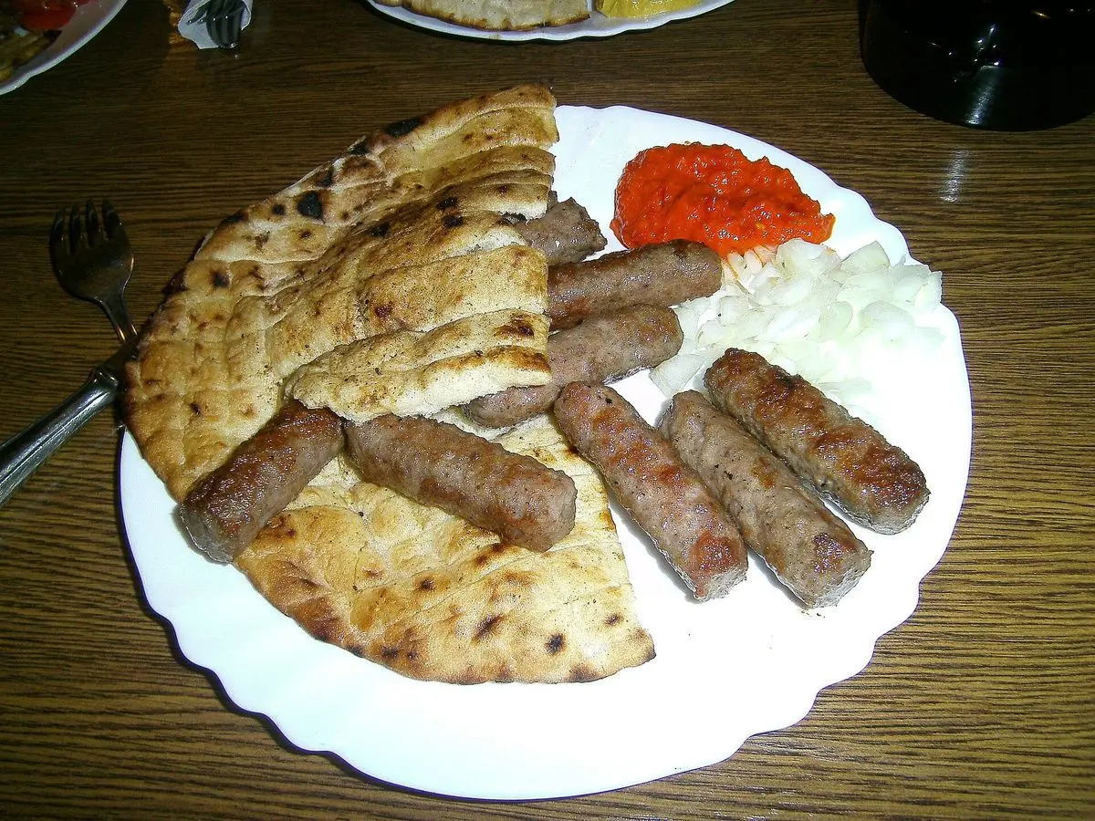 Plato con ćevapčići a la parrilla, pan plano, cebolla picada y salsa de pimiento rojo