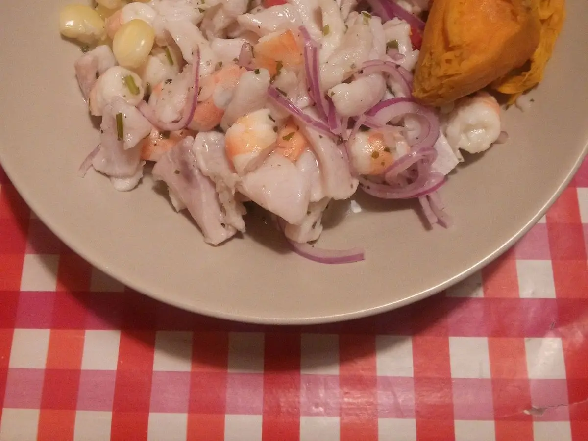 Ceviche de pescado con cebolla morada, maíz choclo desgranado y trozos de boniato en un plato