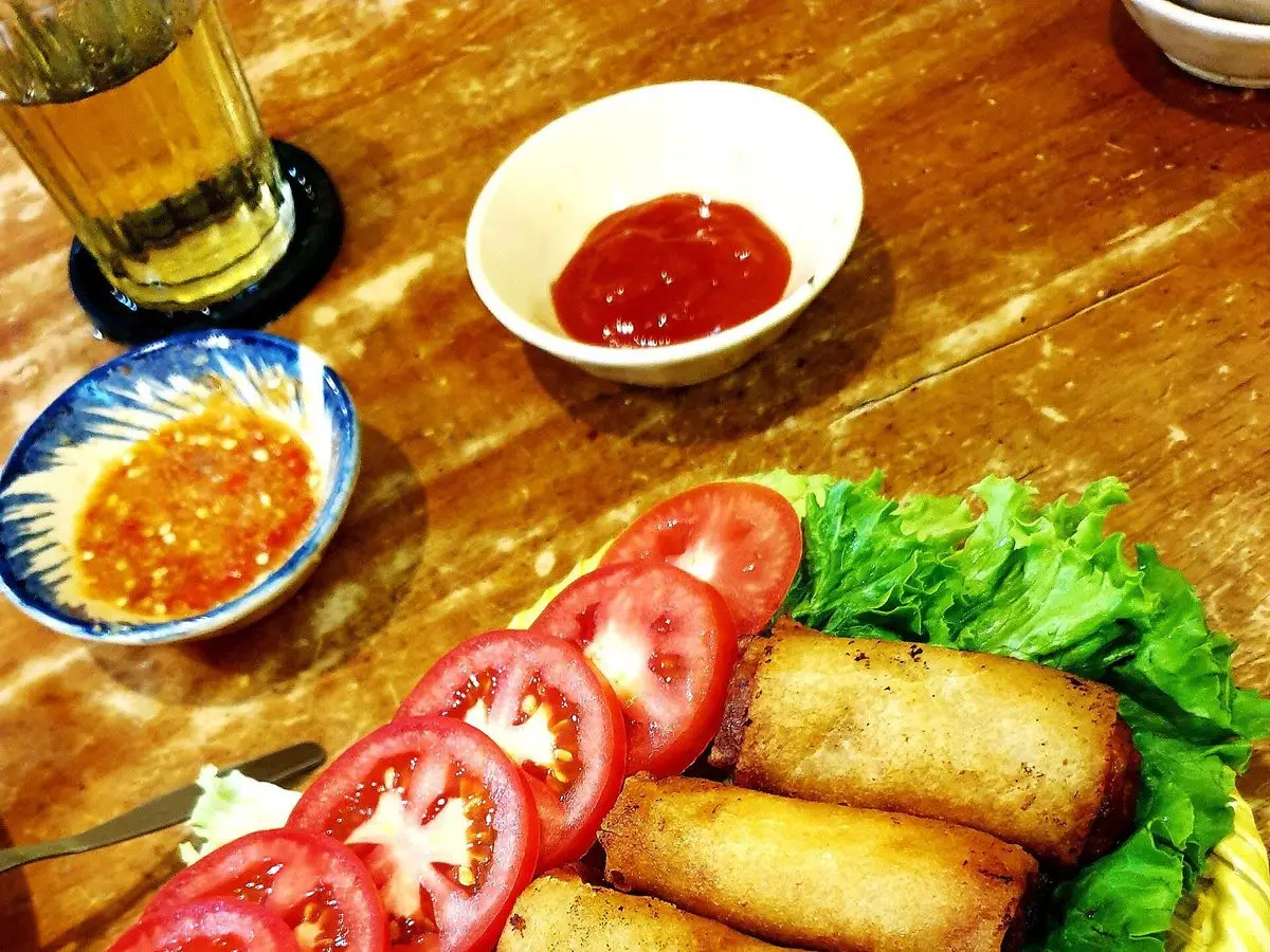 Rollitos vietnamitas fritos y dorados sobre lechuga con rodajas de tomate y salsa dulce picante en un cuenco