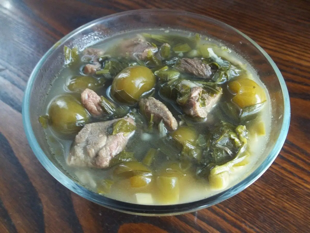 Cuenco de cristal con guiso georgiano de cordero, hierbas verdes y ciruelas verdes en caldo