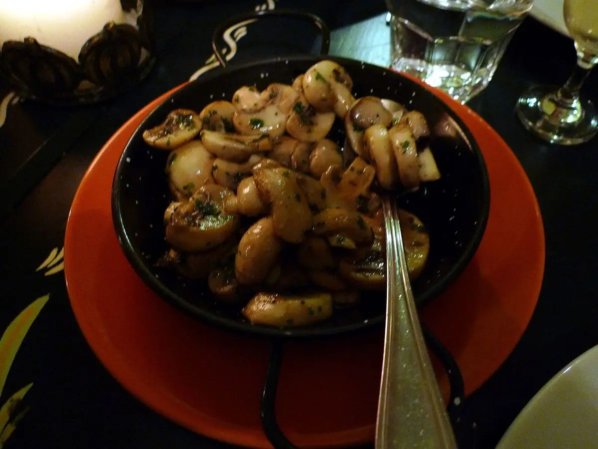 Cazuela negra con champiñones salteados al ajillo y un tenedor, sobre un plato rojo
