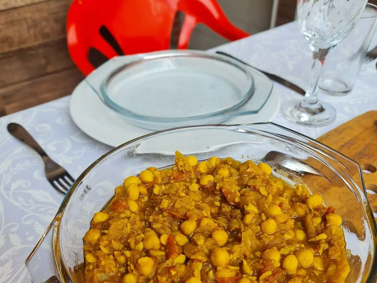 Fuente de cristal con chana masala de garbanzos amarillo anaranjado sobre una mesa puesta