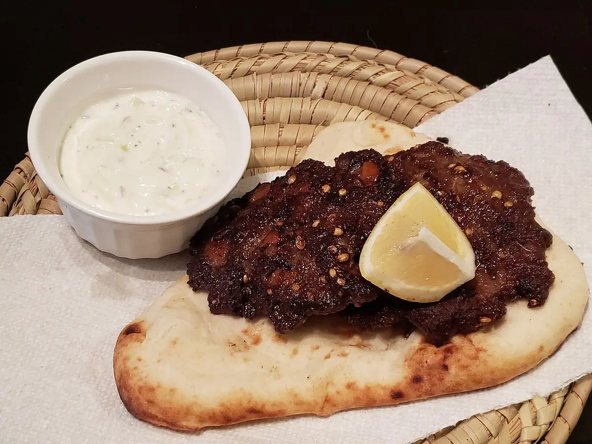 Kebab de carne picada con rodaja de limón sobre pan naan y un cuenco de salsa de yogur