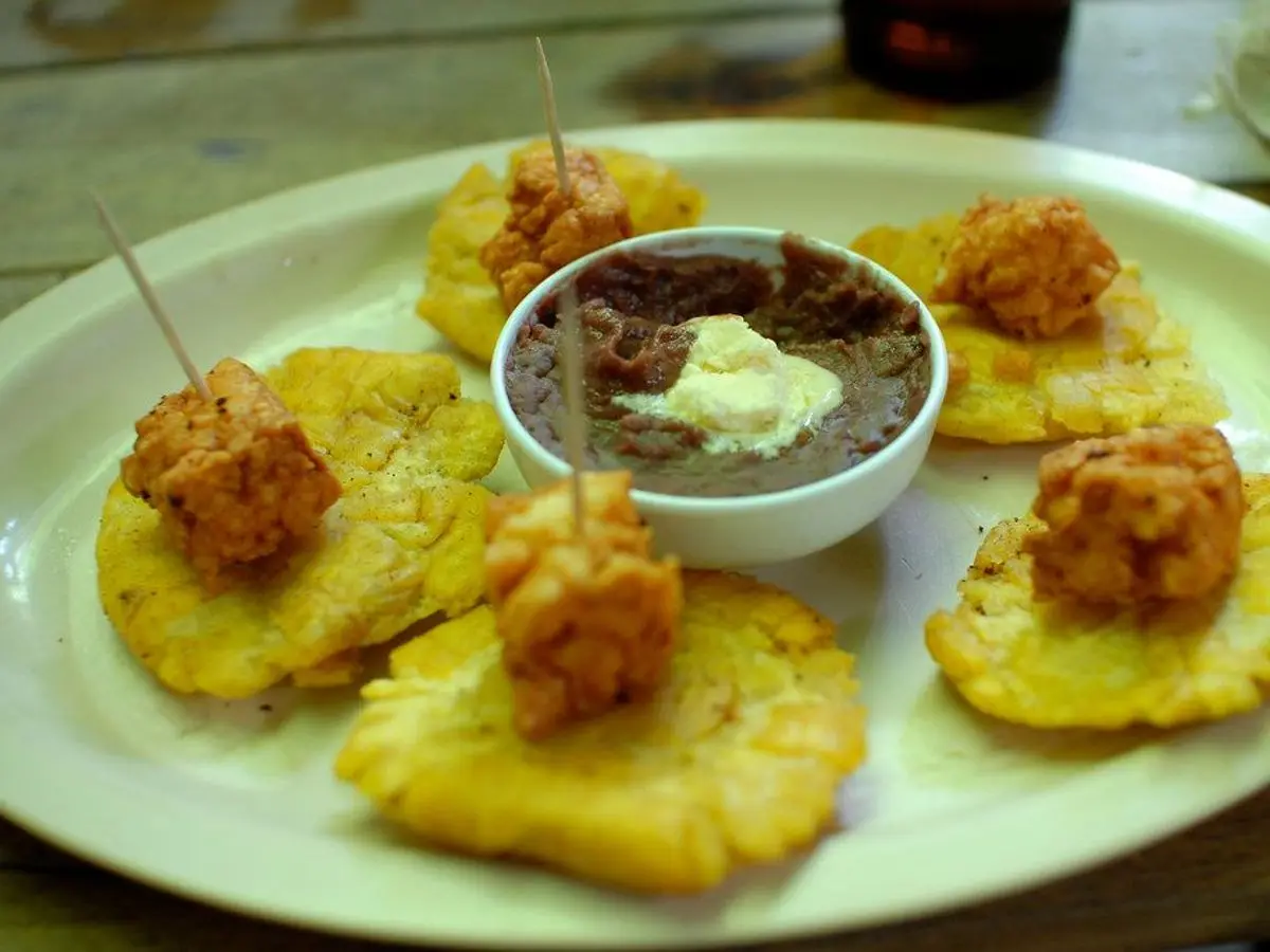 Tostones de plátano dorados con bocados fritos y un cuenco de salsa en un plato blanco
