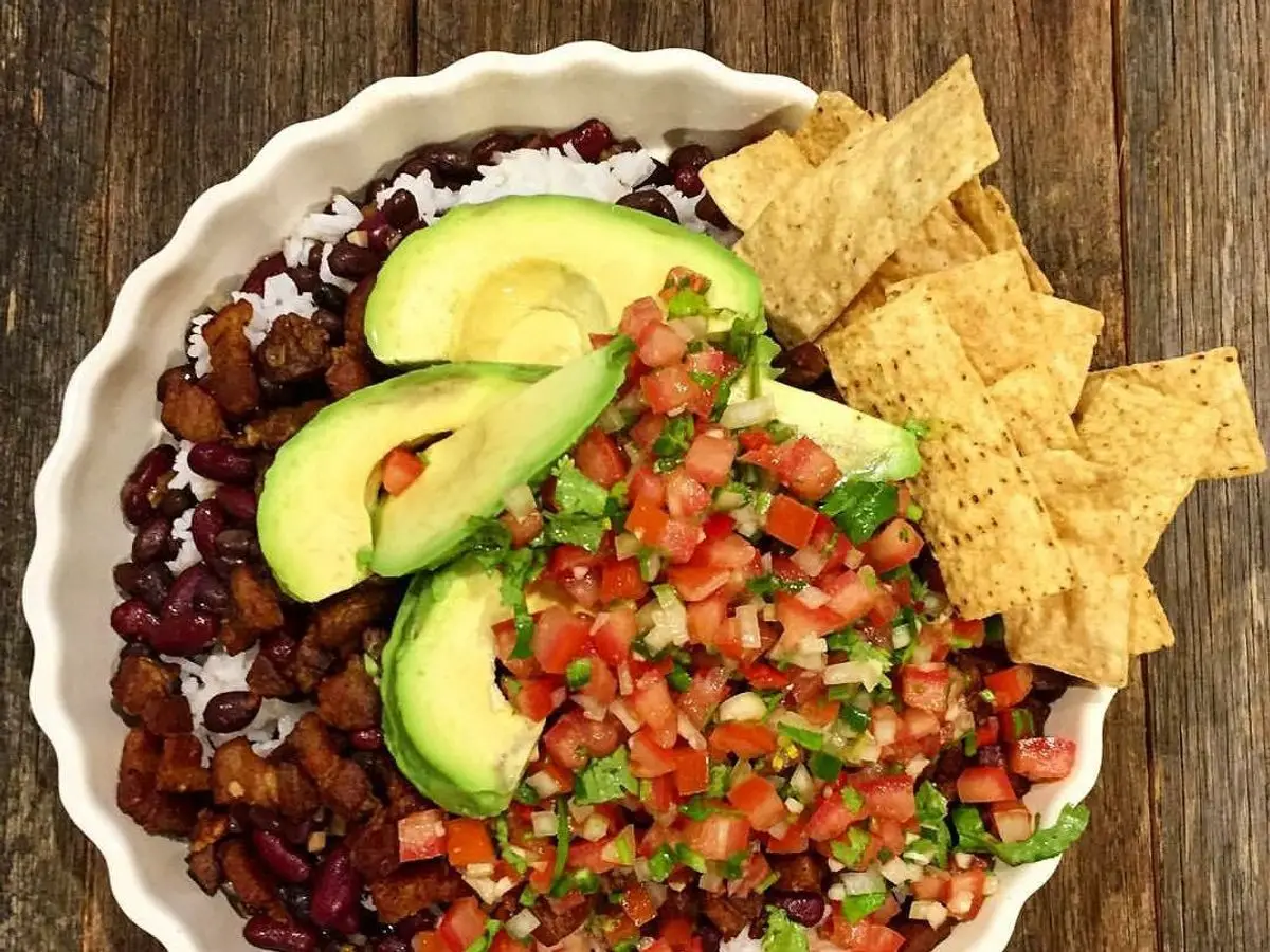 Cuenco de chifrijo con frijoles, pico de gallo, aguacate y nachos sobre mesa de madera