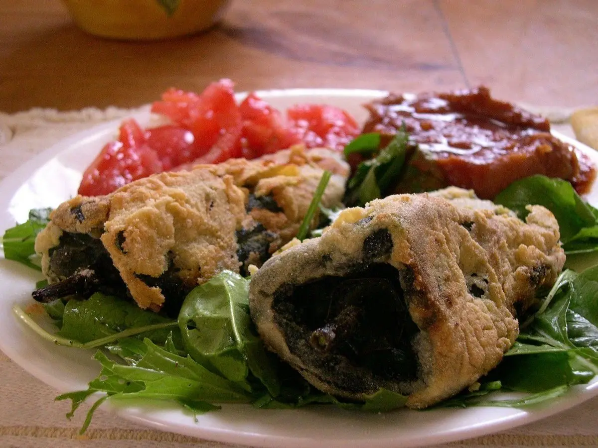 Chiles rellenos abiertos sobre un plato con rúcula, tomate y salsa roja