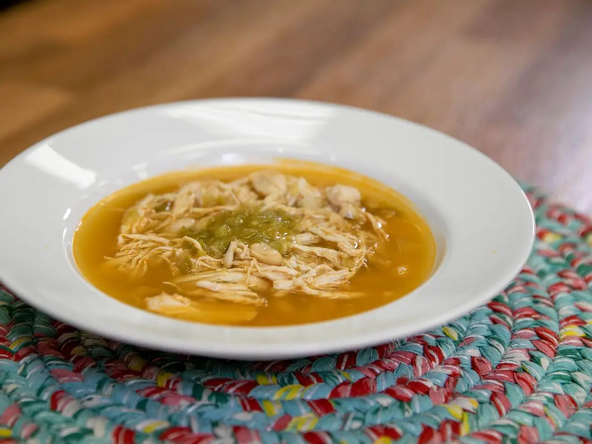 Plato hondo blanco de sopa de pollo desmenuzado con alubias blancas sobre un mantel trenzado de colores