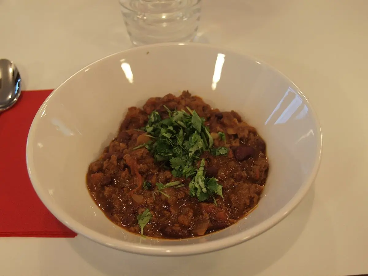 Cuenco blanco de chili con carne con alubias y carne picada decorado con perejil fresco
