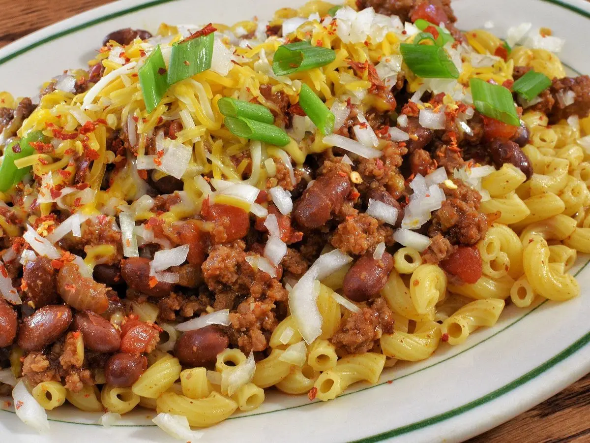 Macarrones con chili de carne y alubias rojas, queso rallado y cebolleta en un plato