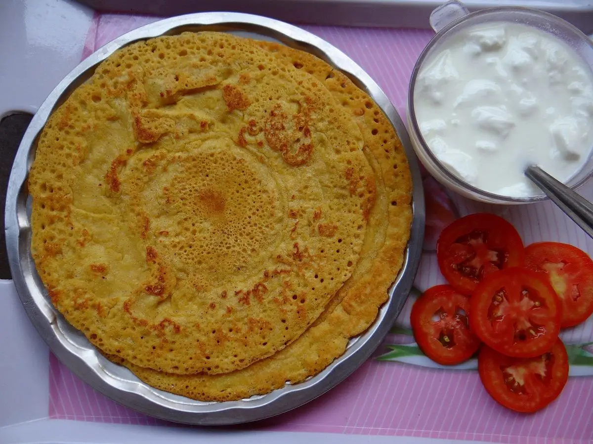 Tortita salada de harina de garbanzo en una bandeja metálica con yogur y rodajas de tomate