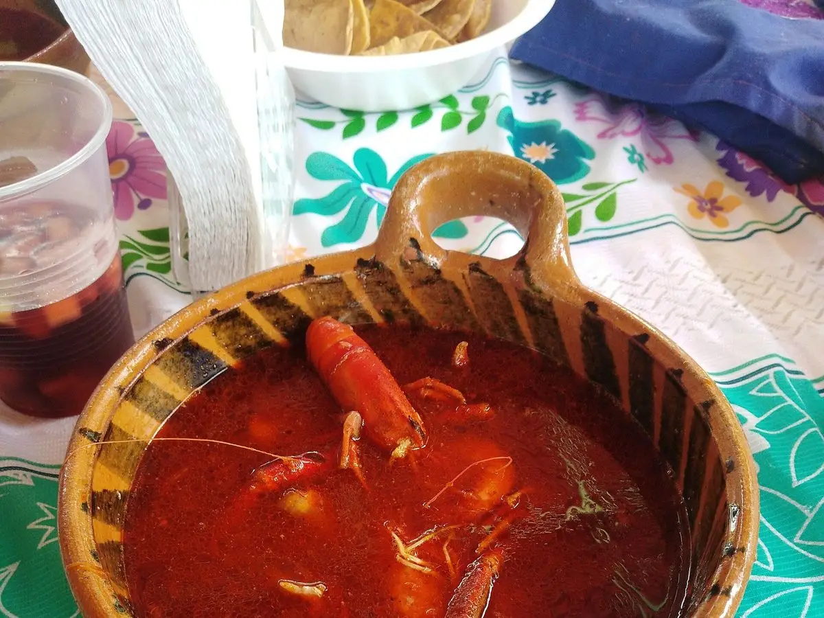 Cazuela de barro con caldo rojo de chilpachole con gambas y marisco sobre mantel verde