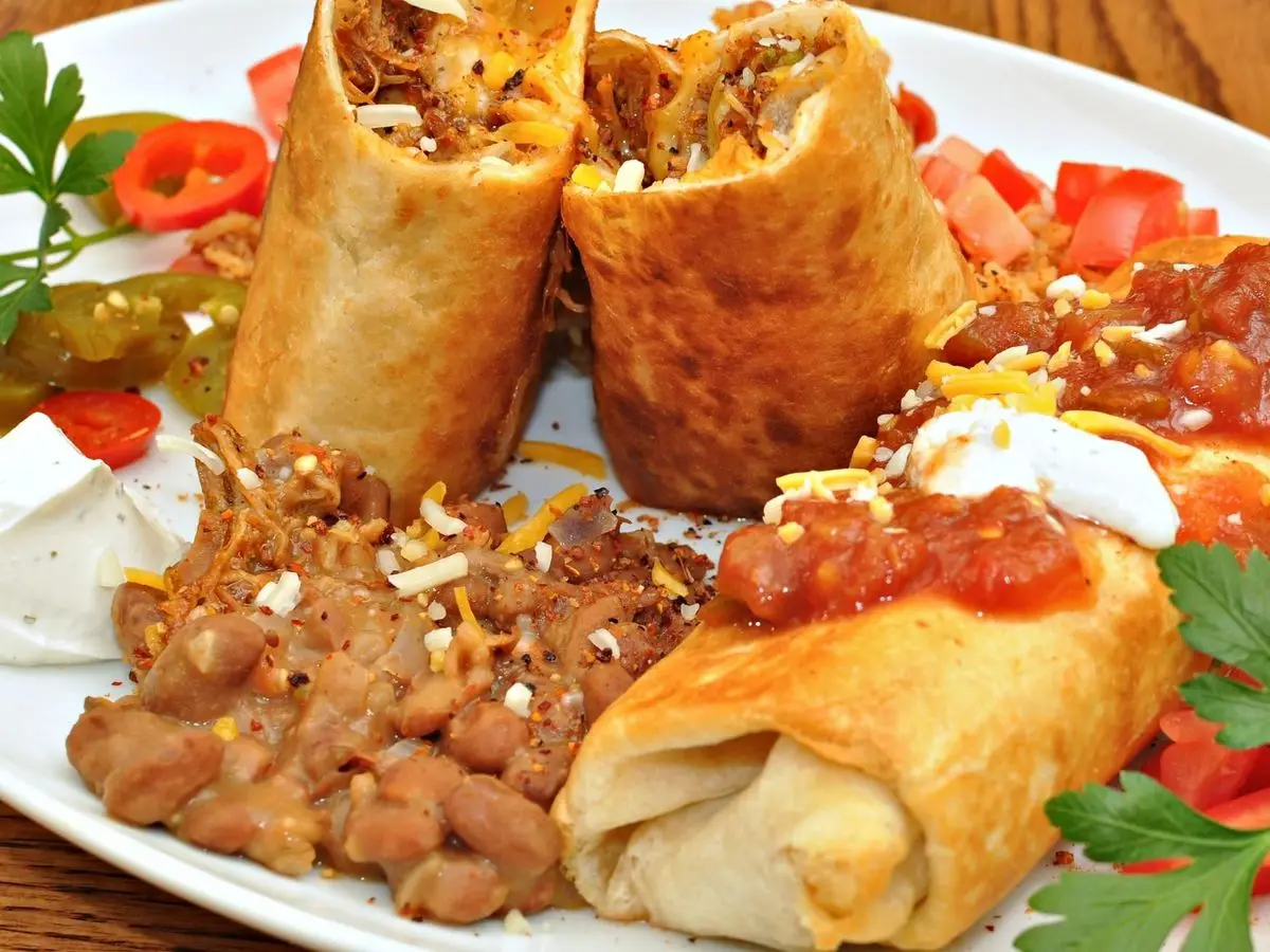 Chimichangas doradas con frijoles pintos, pico de gallo, crema agria y perejil en un plato blanco