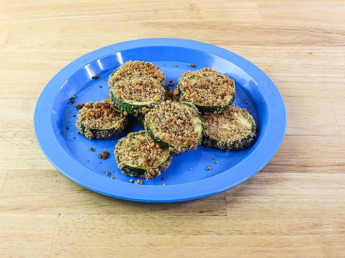 Rodajas de calabacín rebozadas y horneadas sobre un plato azul