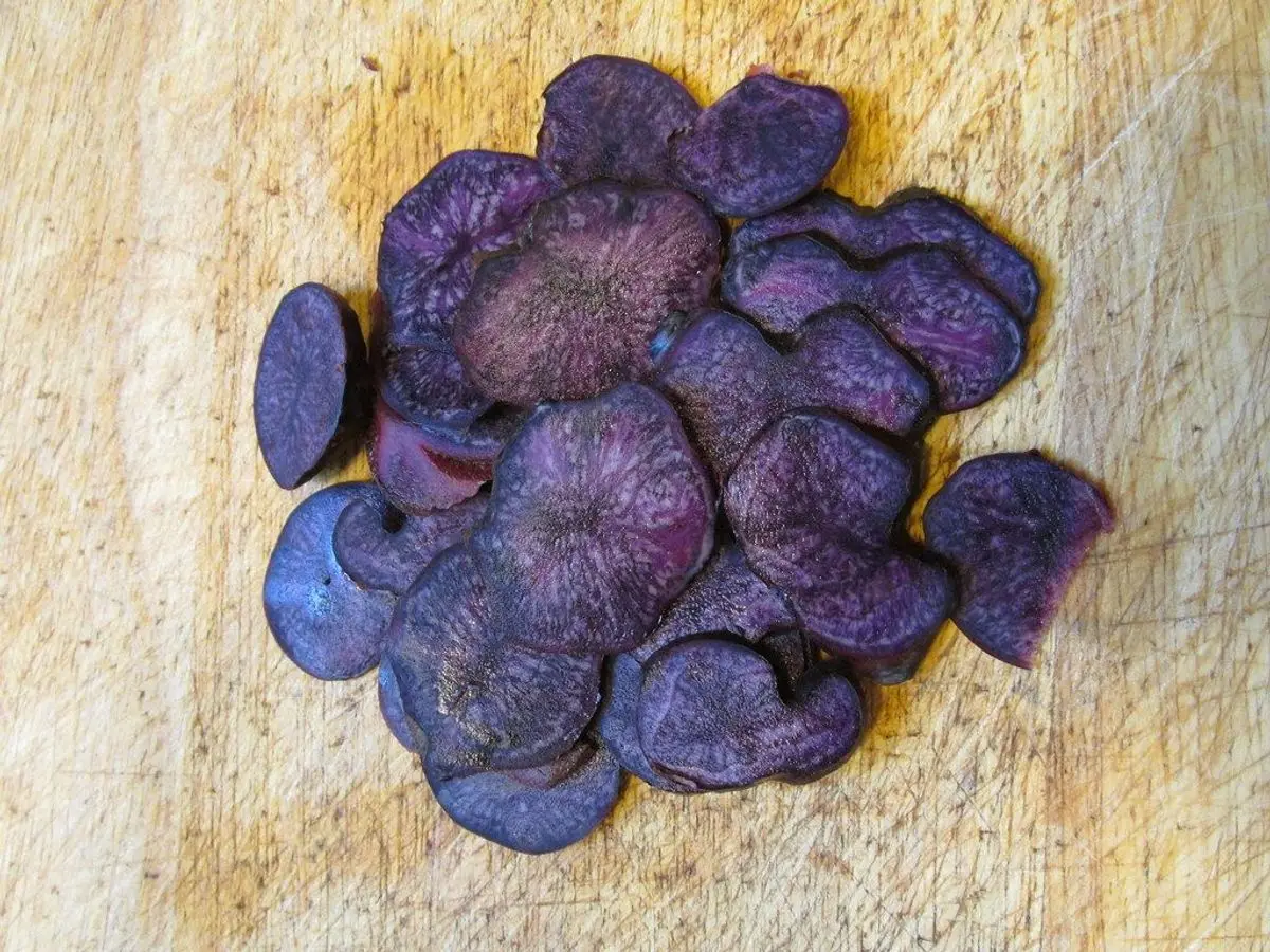 Rodajas finas de patata violeta dispuestas sobre una tabla de madera