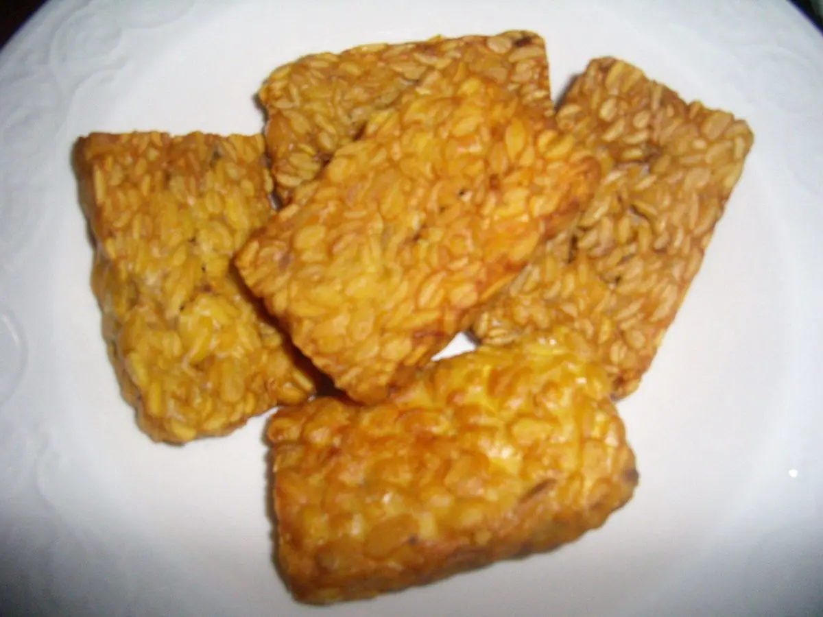 Lonchas de tempeh doradas y crujientes, con su grano a la vista, sobre un plato blanco