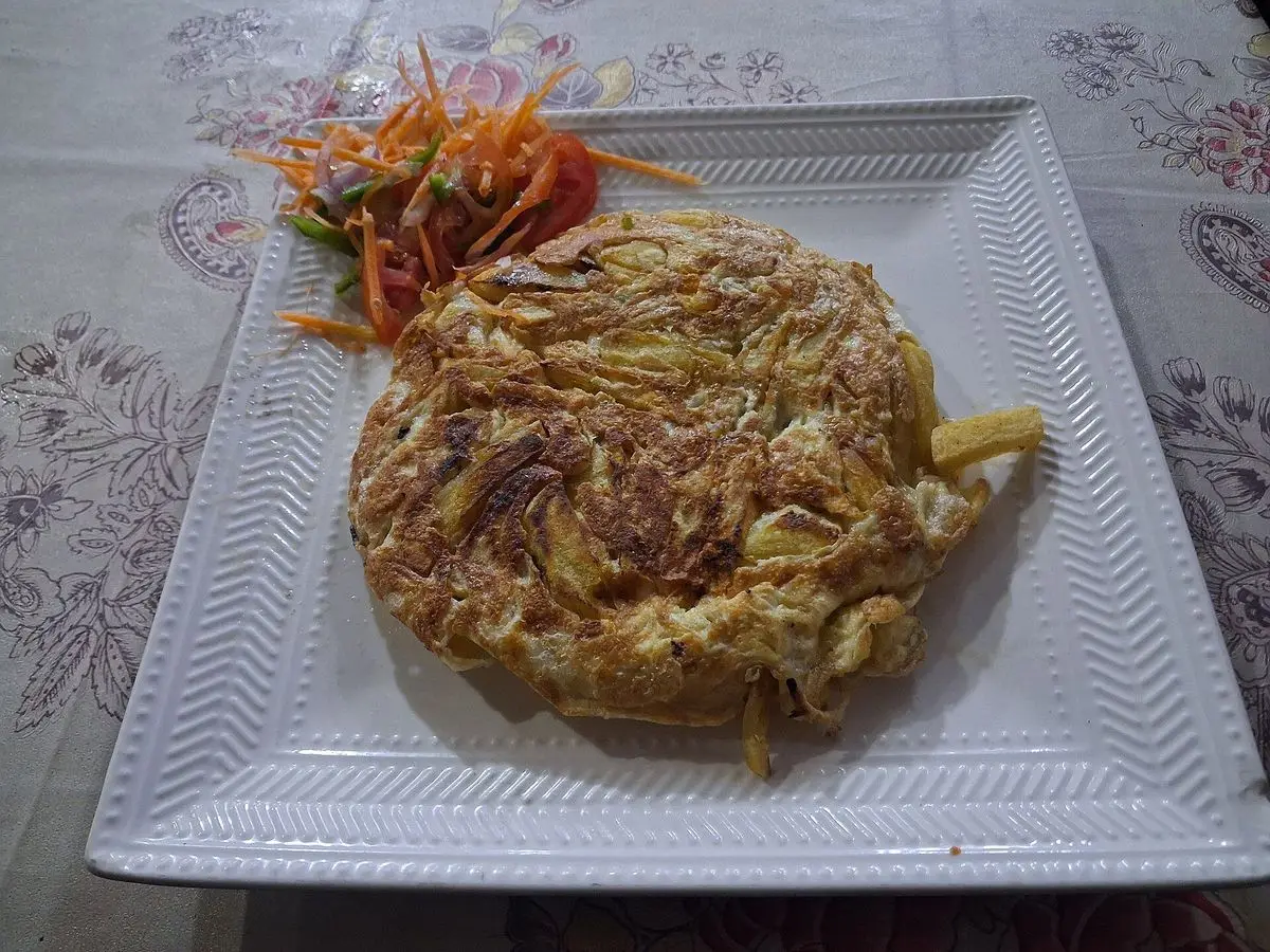 Tortilla de patatas fritas dorada con ensalada de zanahoria rallada sobre un plato cuadrado blanco