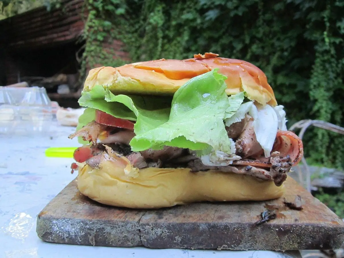 Sándwich chivito de ternera con lechuga, tomate, huevo y queso sobre una tabla de piedra