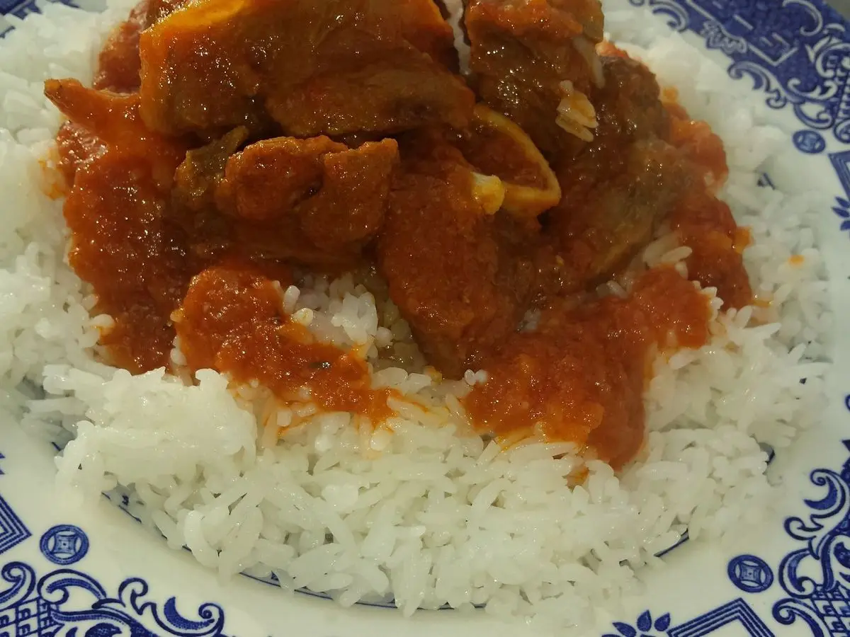Guiso de carne de cabrito en salsa de tomate sobre arroz blanco en plato decorado