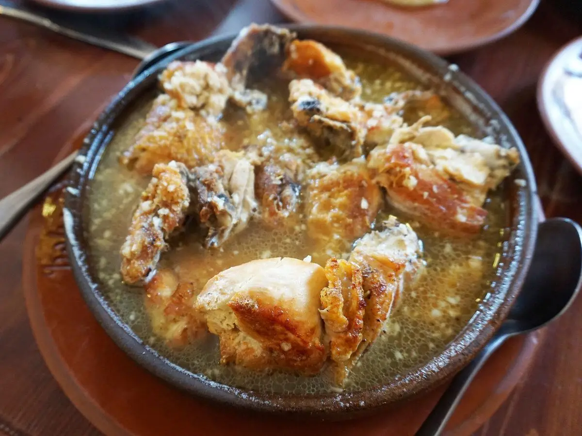 Pollo pequeño dorado en una sartén de hierro con salsa cremosa de ajo y leche sobre una mesa de madera