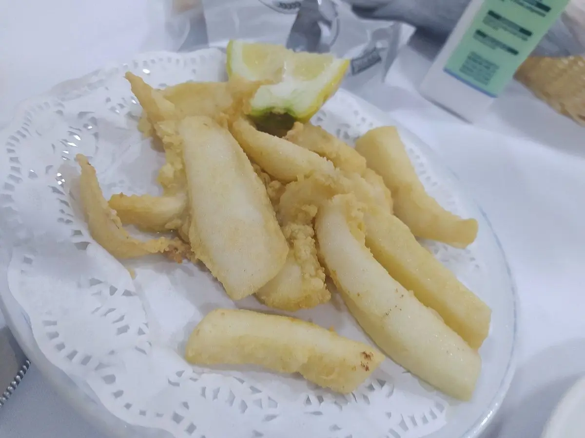 Tiras de sepia rebozadas y fritas con gajos de limón sobre un plato de papel calado