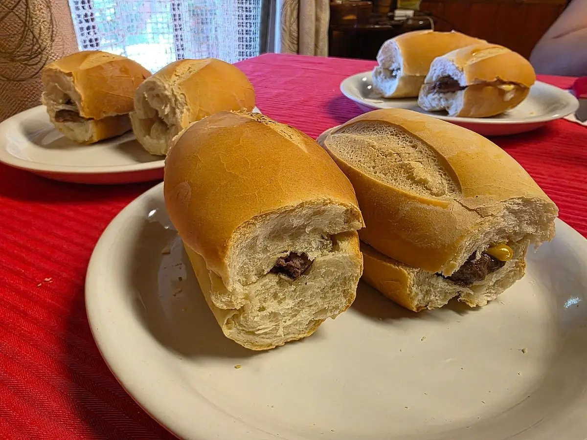 Choripanes en panecillos alargados servidos en platos blancos sobre un mantel rojo