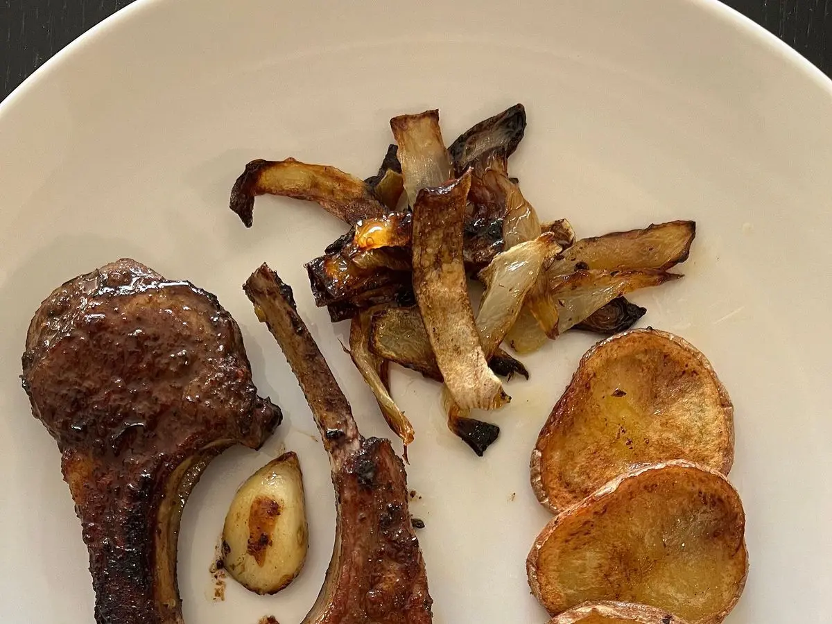 Chuletas de cordero doradas con rodajas de patata frita y cebolla pochada