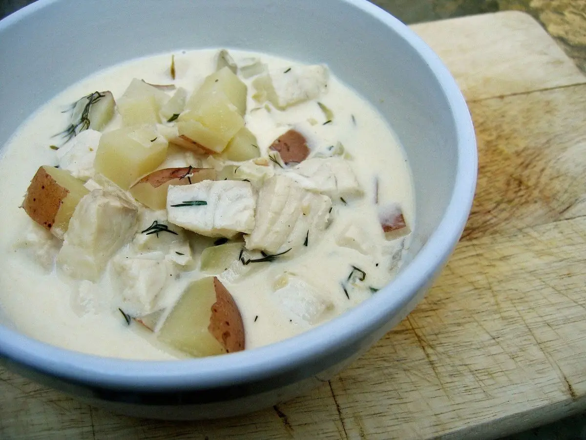 Cuenco de sopa cremosa de pescado con trozos de patata y eneldo sobre una tabla de madera