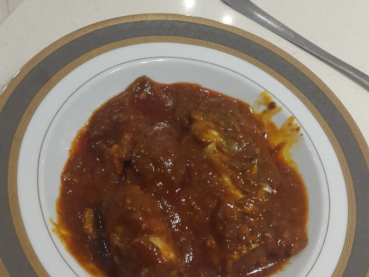 Plato con pescado guisado en espesa salsa roja de tomate y especias, con borde dorado y gris