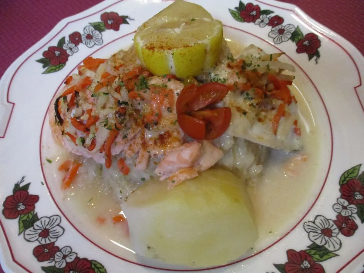 Pescado con chucrut, zanahoria, patata cocida y rodaja de limón en un plato de porcelana floral