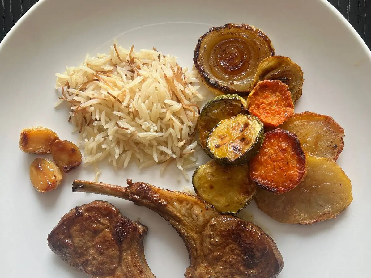 Chuletas de cordero a la plancha con arroz y verduras asadas en un plato blanco
