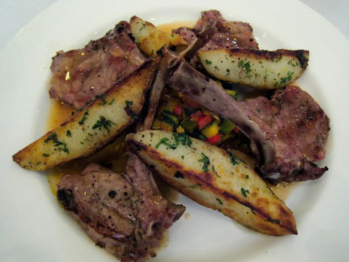Chuletas de cordero a la plancha con gajos de patata asada y hierbas en un plato blanco