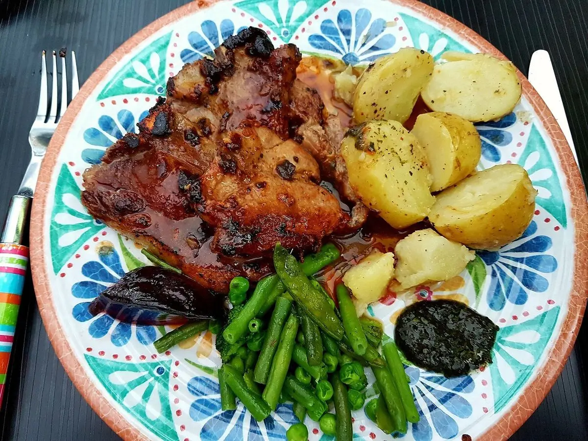 Chuletas de cordero doradas con patatas nuevas salteadas y judías verdes en un plato de colores