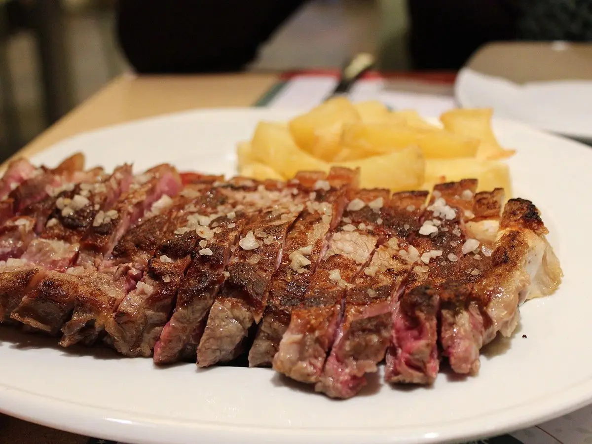 Chuletón de vaca a la parrilla cortado en lonchas con sal en escamas y patatas fritas