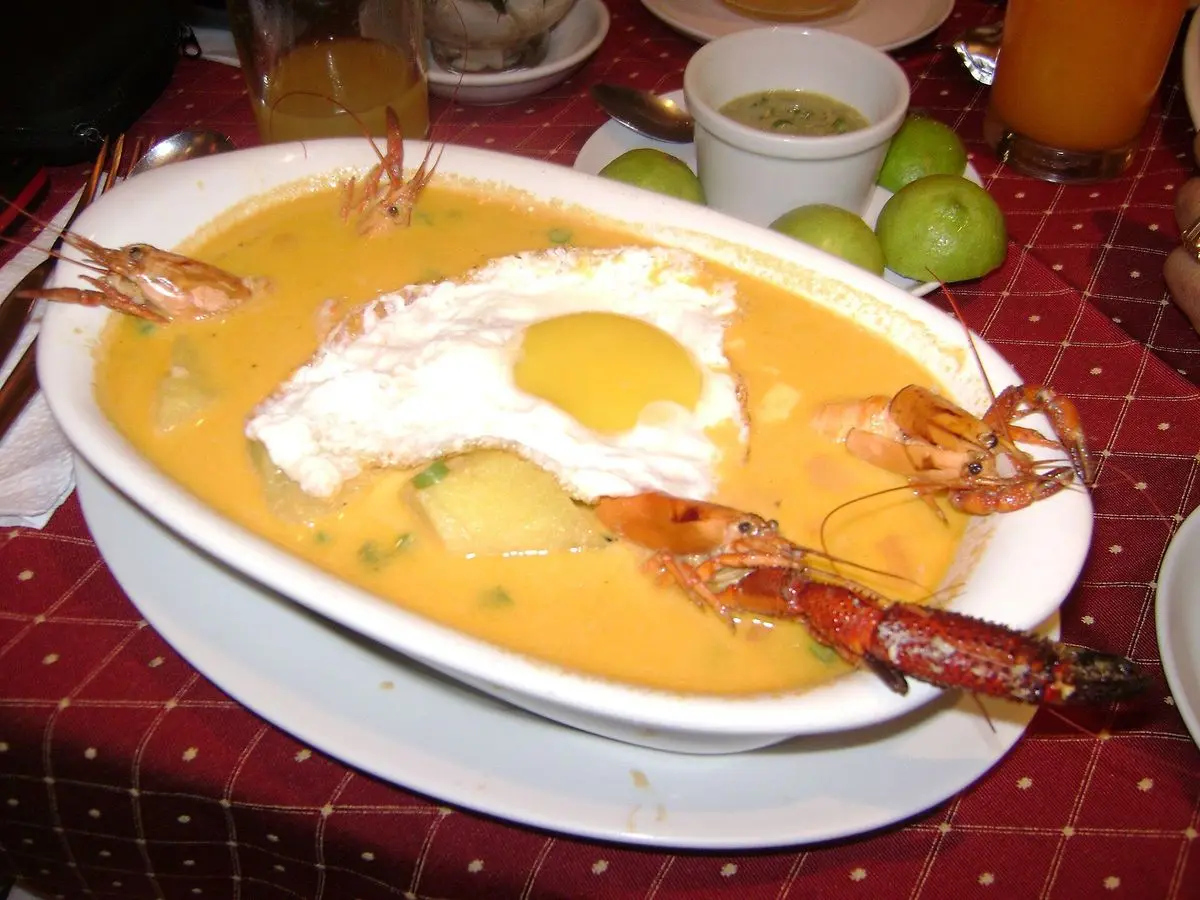 Fuente de chupe cremoso con huevo frito, langostinos enteros y patata sobre mantel de cuadros rojos