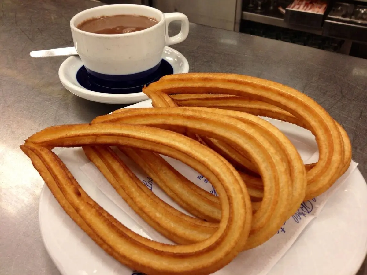 Churros dorados en un plato junto a una taza de chocolate caliente