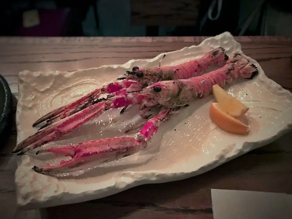 Cigalas a la plancha sobre una bandeja alargada blanca con gajos de limón