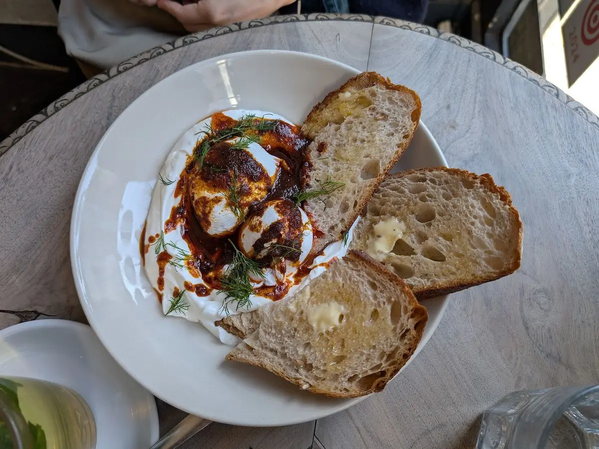 Huevos pochados sobre yogur con aceite de pimentón y rebanadas de pan en un plato blanco