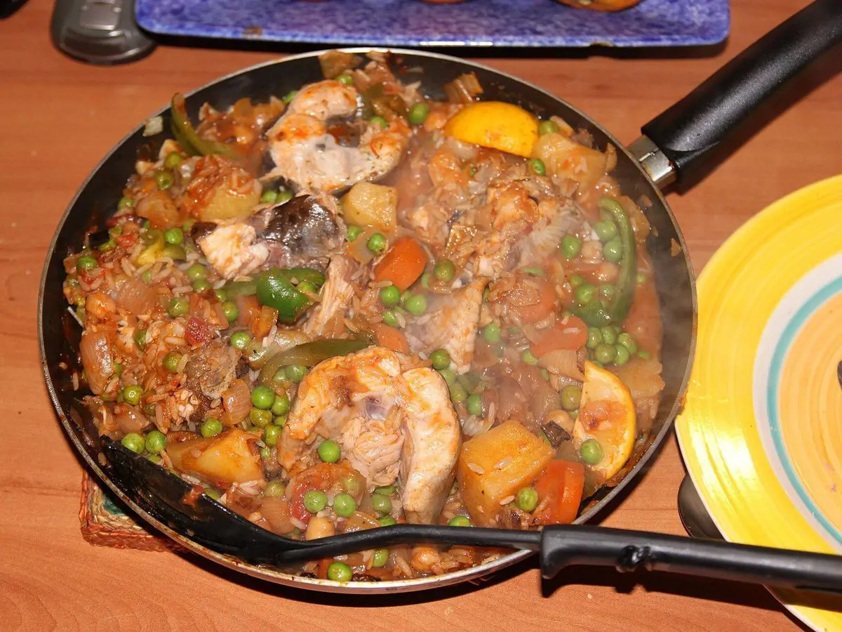 Sartén con guiso de rodajas de pescado blanco, patata, guisantes, zanahoria y pimiento verde en salsa de tomate