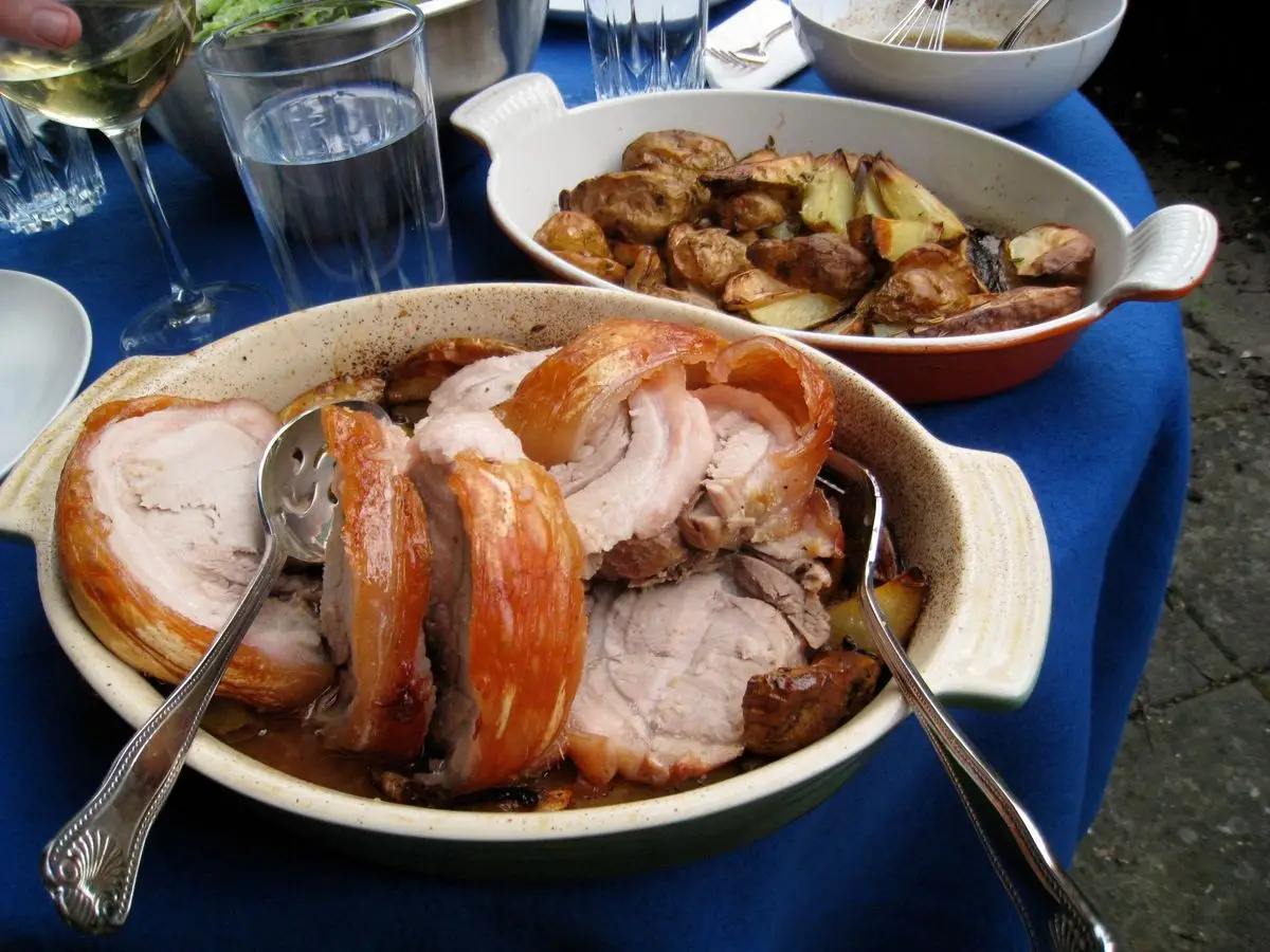 Fuente con lomo de cerdo asado en lonchas junto a patatas asadas sobre un mantel azul