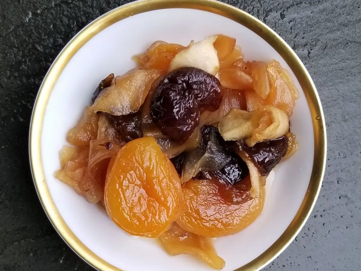 Plato con ciruelas pasas y orejones cocidos en su jugo, sobre un plato de borde dorado