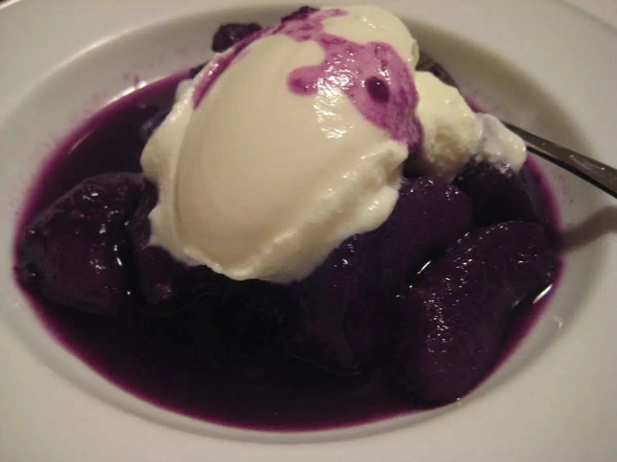 Cuenco blanco con ciruelas guisadas de color morado y una bola de yogur cremoso encima