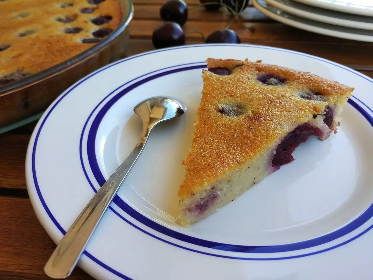 Porción de clafoutis de cerezas en un plato blanco de borde azul con una cuchara