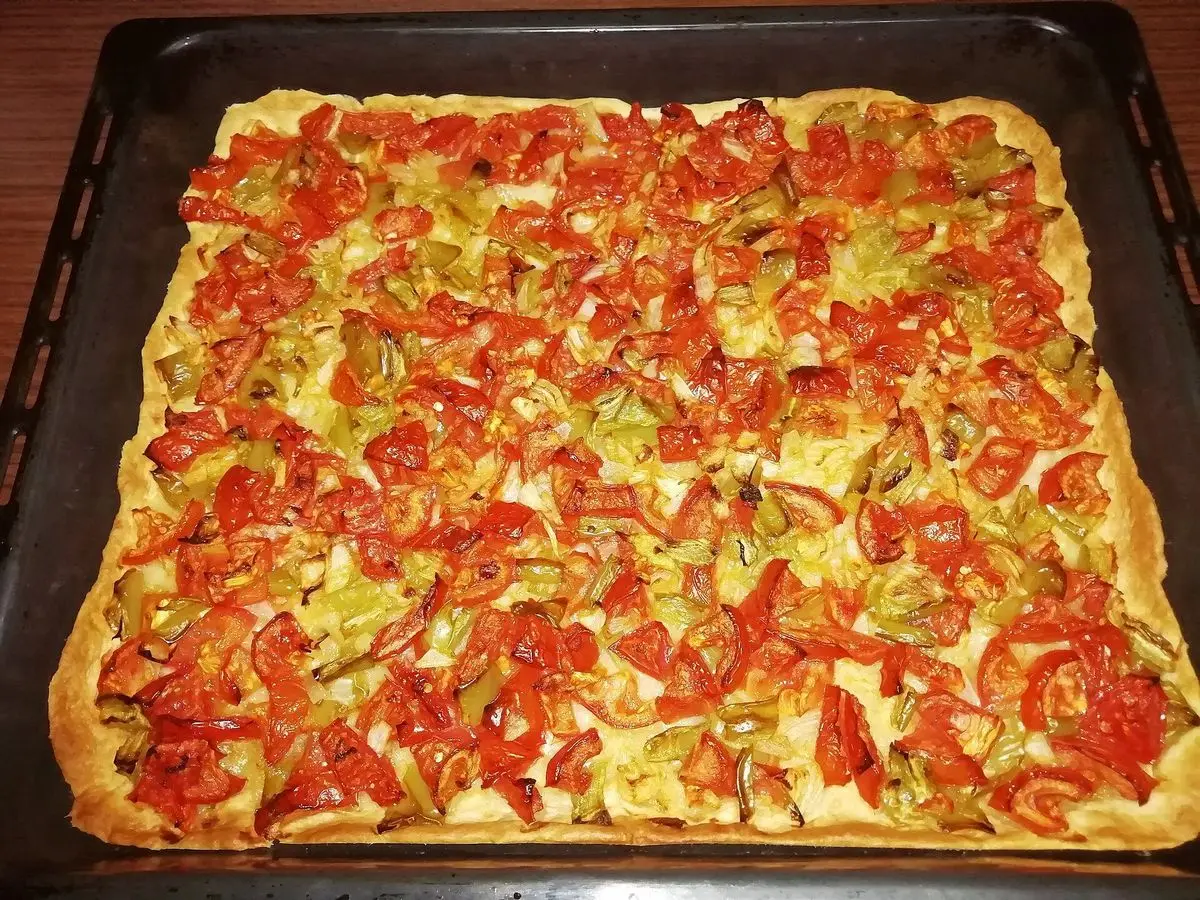 Coca de trempó mallorquina en bandeja de horno, cubierta de tomate, pimiento verde y cebolla