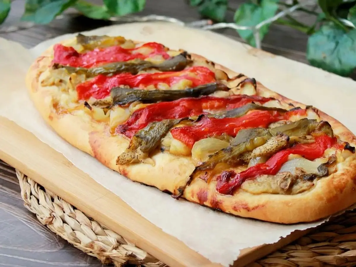 Coca alargada de masa fina con pimiento rojo asado y berenjena sobre papel de horno